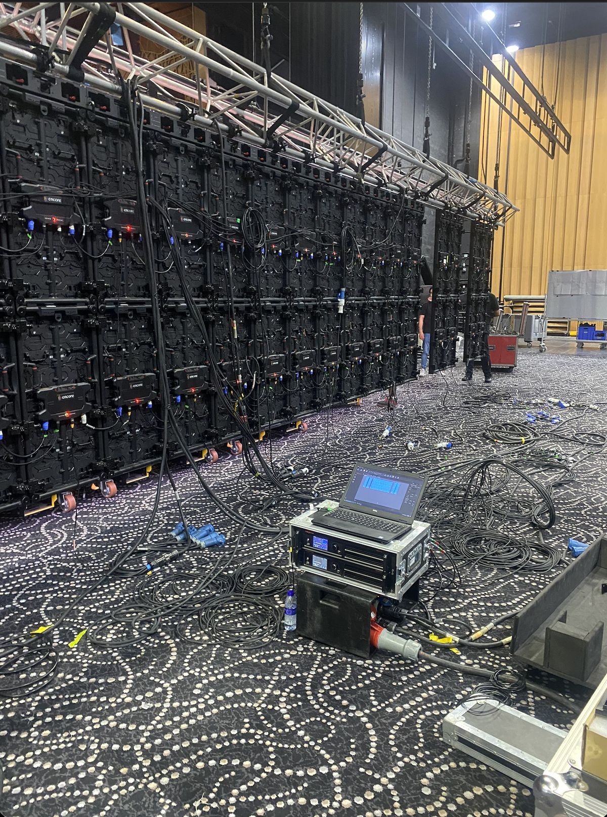 Large-format LED video wall being rigged on truss with cabling laid out across the venue floor